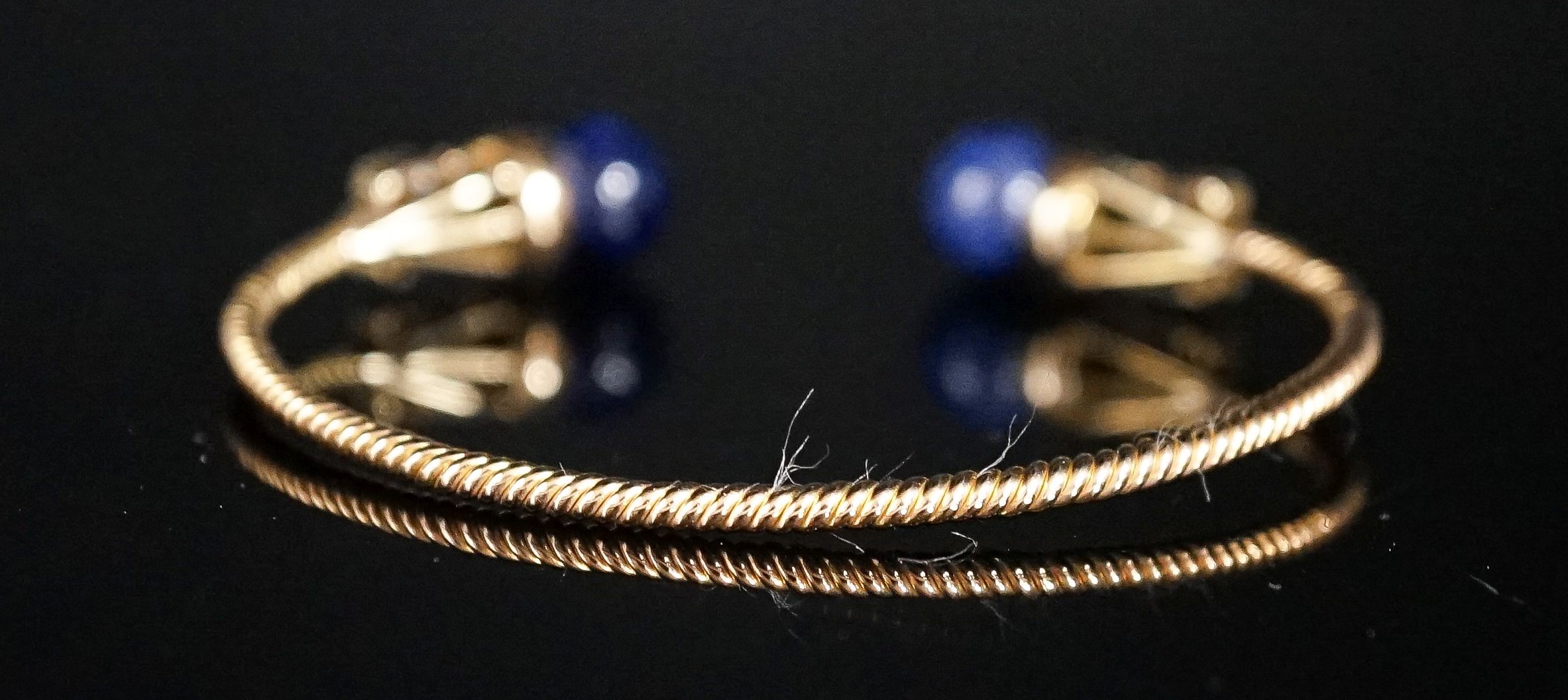 A modern yellow metal twist, two stone sodalite? and diamond set open bangle, gross weight 14 grams.